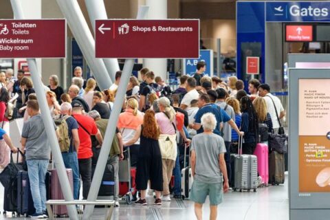 Reisende warten im Flughafen Düsseldorf vor Check-in-Schaltern.